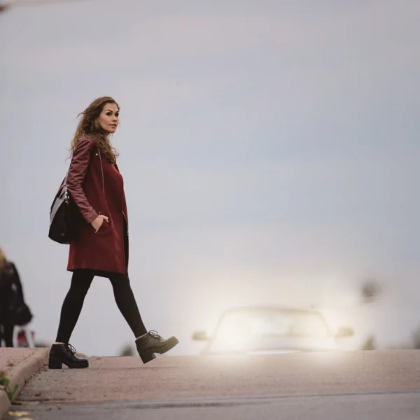 Piéton traversant la route face aux phares d’une voiture, illustrant l’indemnisation d’une victime non conductrice après un accident de la circulation